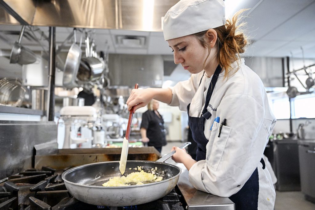 A culinary arts student scrambles eggs in a kitchen setting.
