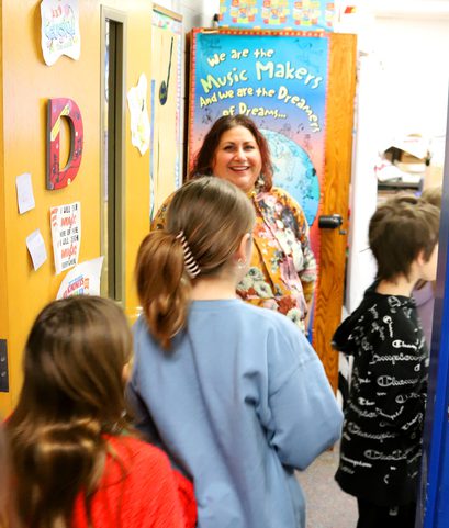 A teacher greets students as they enter her classroom.