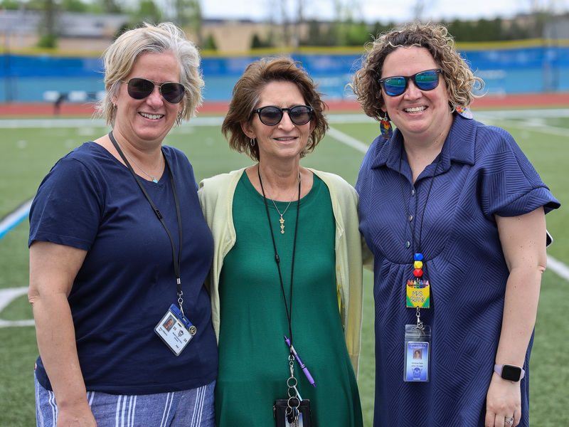 Three teachers pose together on the athletic field.