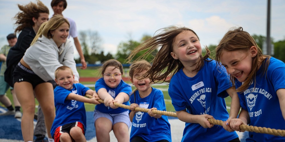 Young and older children pull on a rope during a tug of war game.